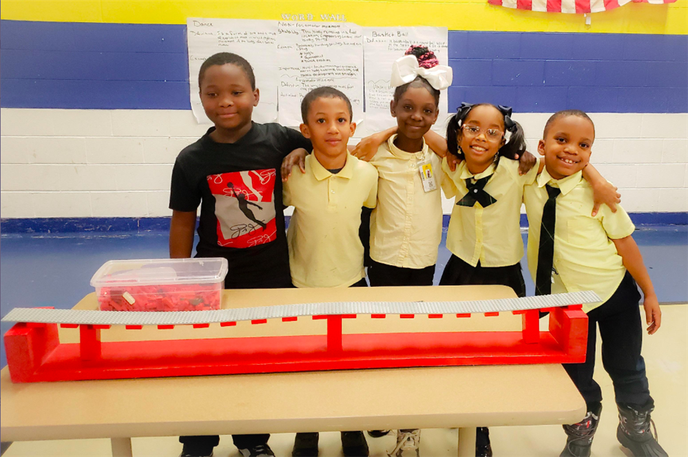  5 students standing behind their lego bridge with arms around each other